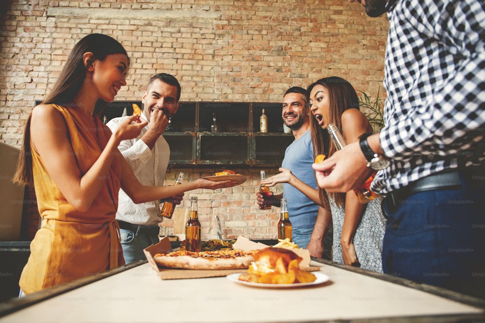 Hausparty. Volle Länge von fröhlichen jungen Leuten, die die Hausparty genießen, während sie kommunizieren und Snacks in der Küche essen