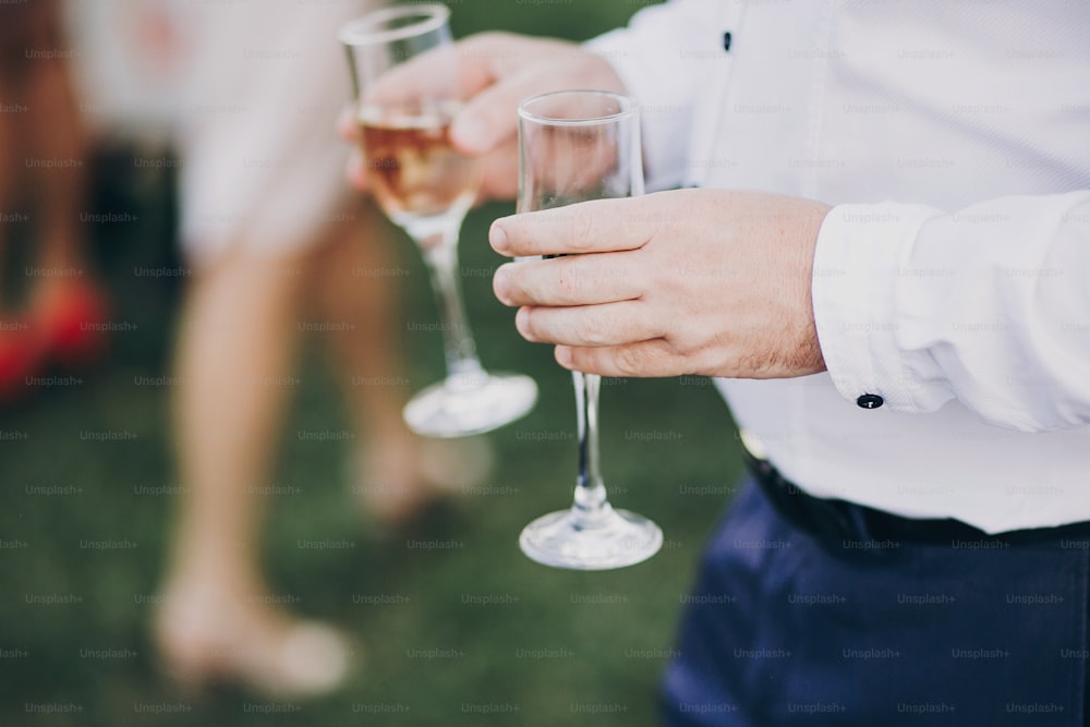 hands of stylish people cheering with glasses of champagne, luxury wedding reception, rich celebration.  guests toasting at christmas luxury celebration feast