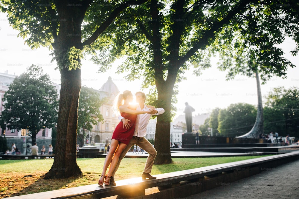 Schönes, glückliches verliebtes Paar, das sich umarmt und in der Abendsonne in der sonnigen Straße tanzt. Stilvoller Hipster-Bräutigam und blonde Braut tanzen, professionelle Tänzer. Romantische Momente im Sommer