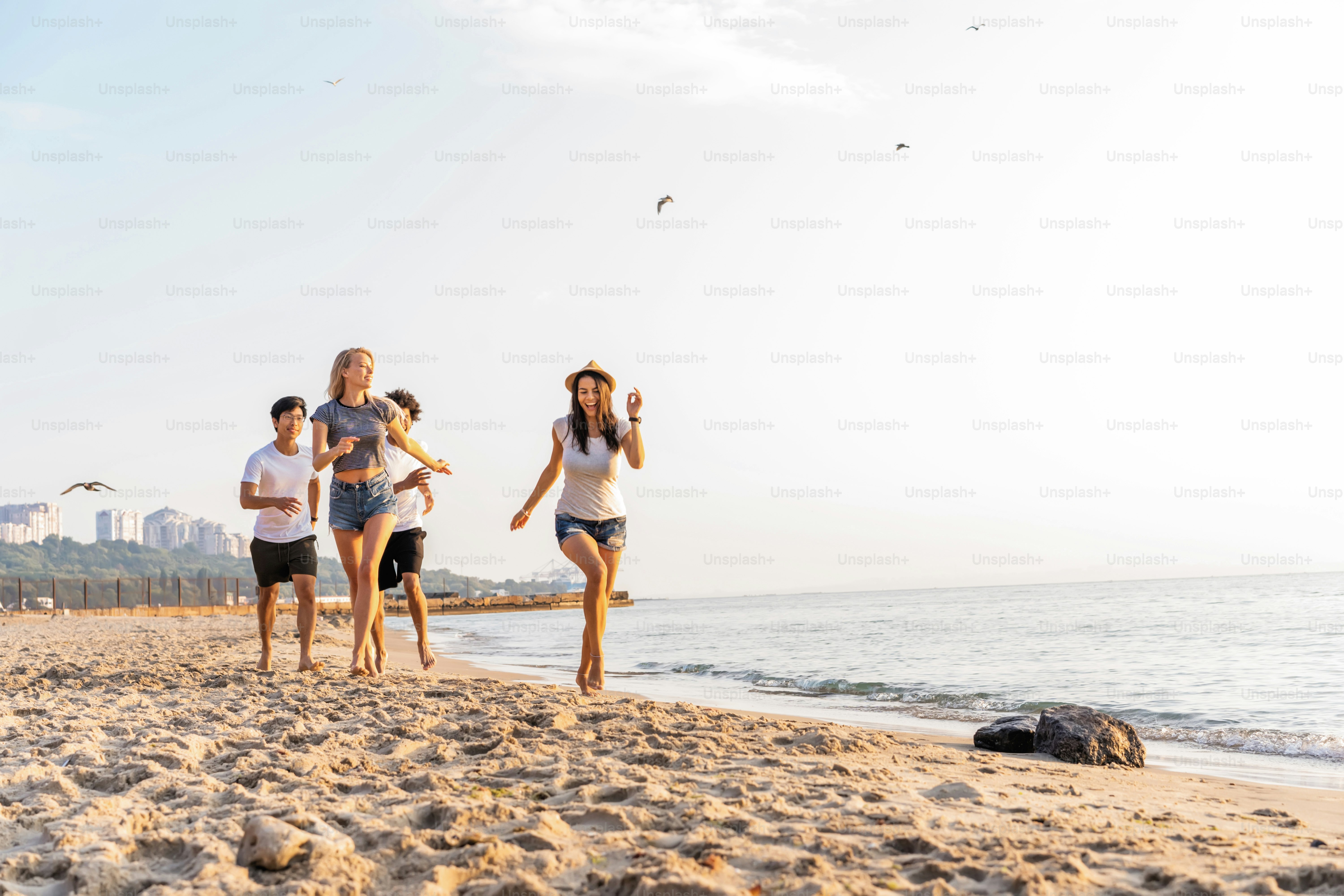 Group of friends having fun running down the beach at sunset