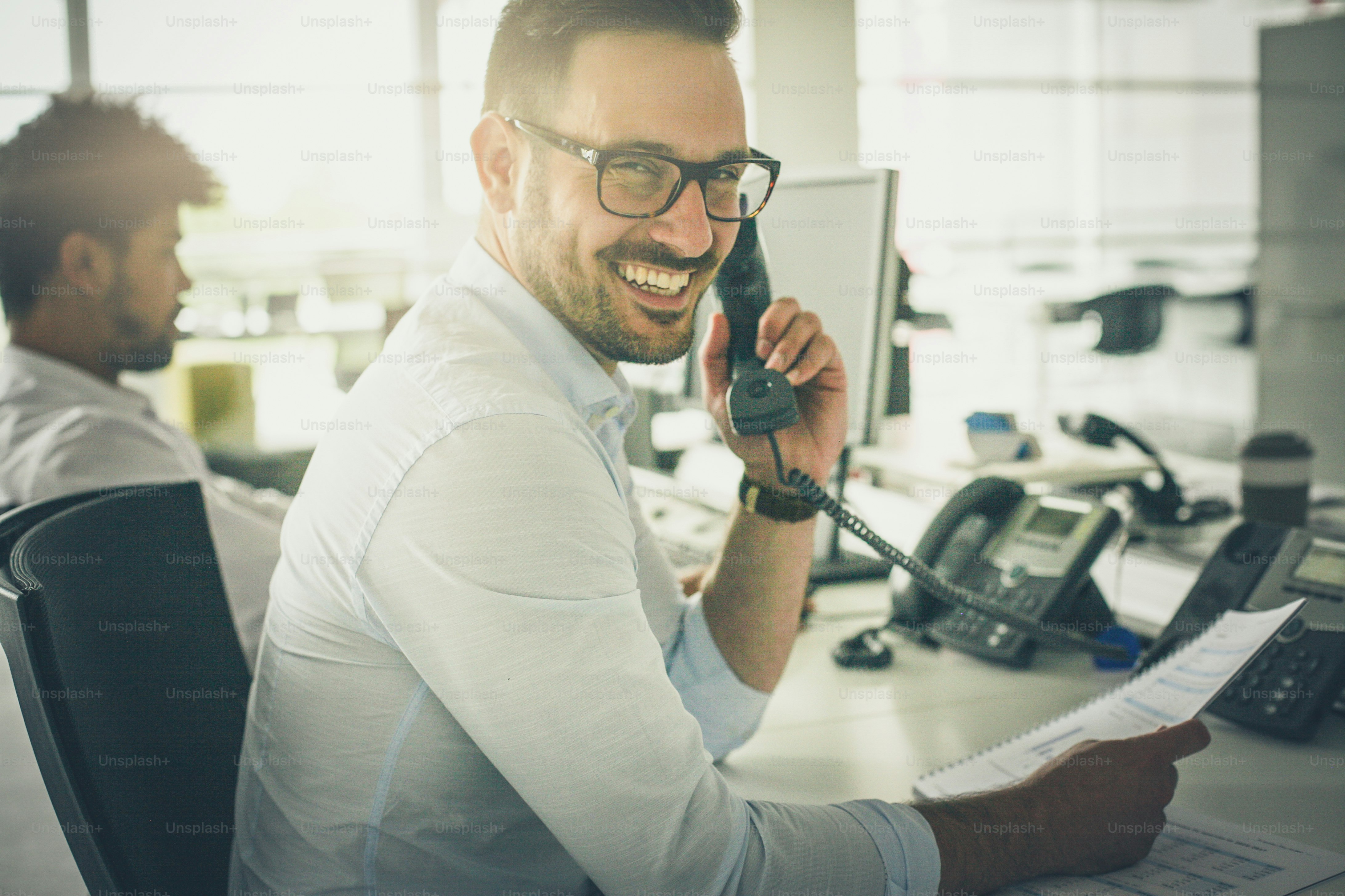 Answer at any moment. Business man having conversation on Landline phone. Looking at camera. Focus on foreground.