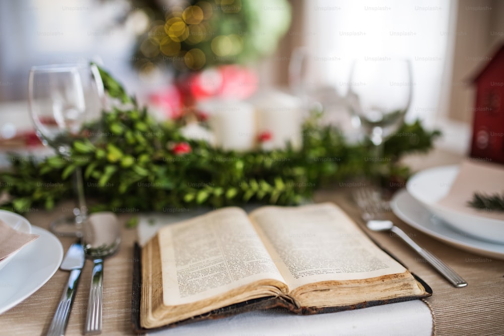 Libro sacro biblico aperto su una tavola apparecchiata per una cena a casa nel periodo natalizio.
