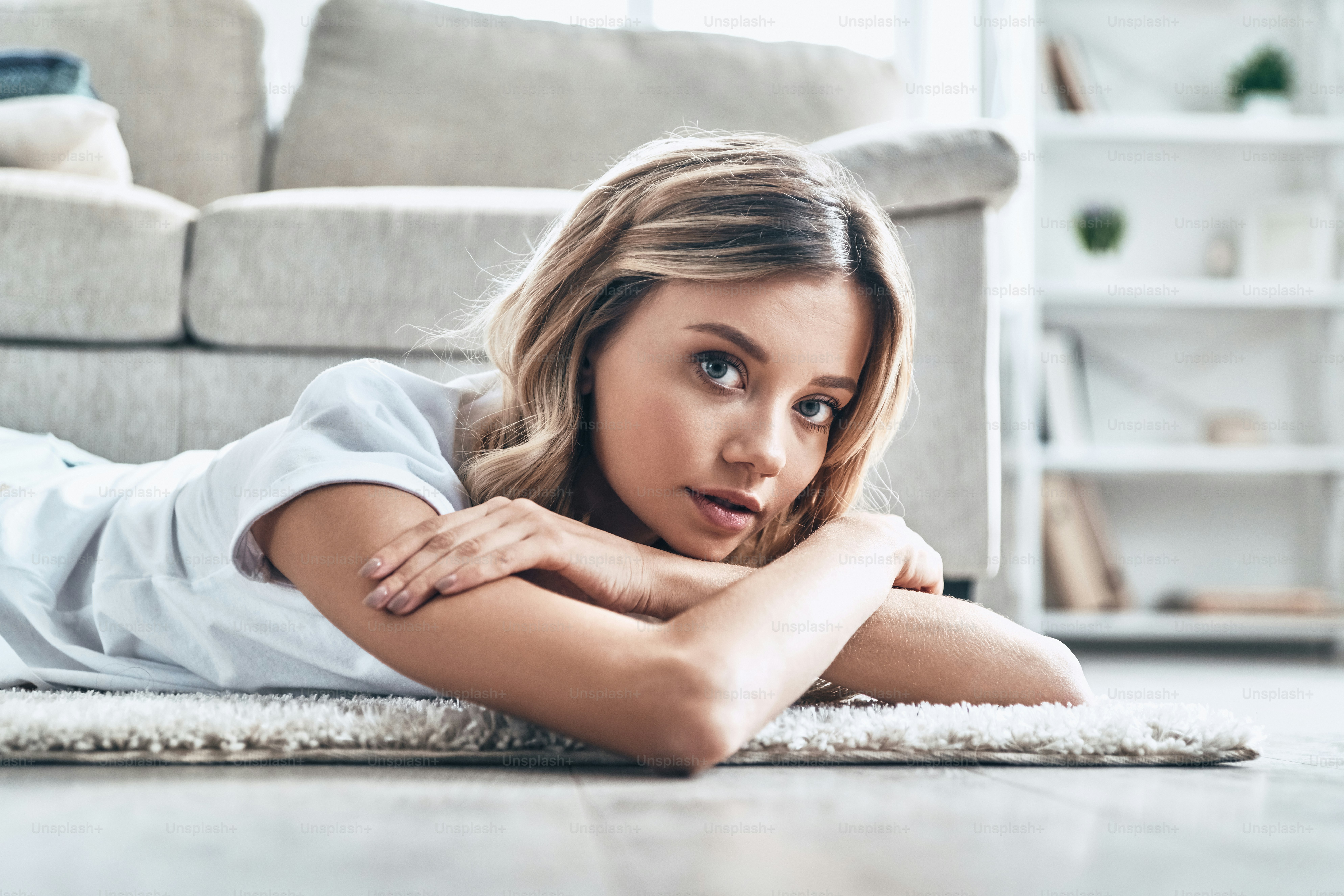 Bella giovane donna che guarda la macchina fotografica e sorride mentre si trova sul pavimento a casa