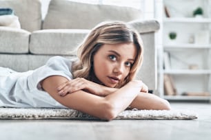 Beautiful young woman looking at camera and smiling while lying on the floor at home
