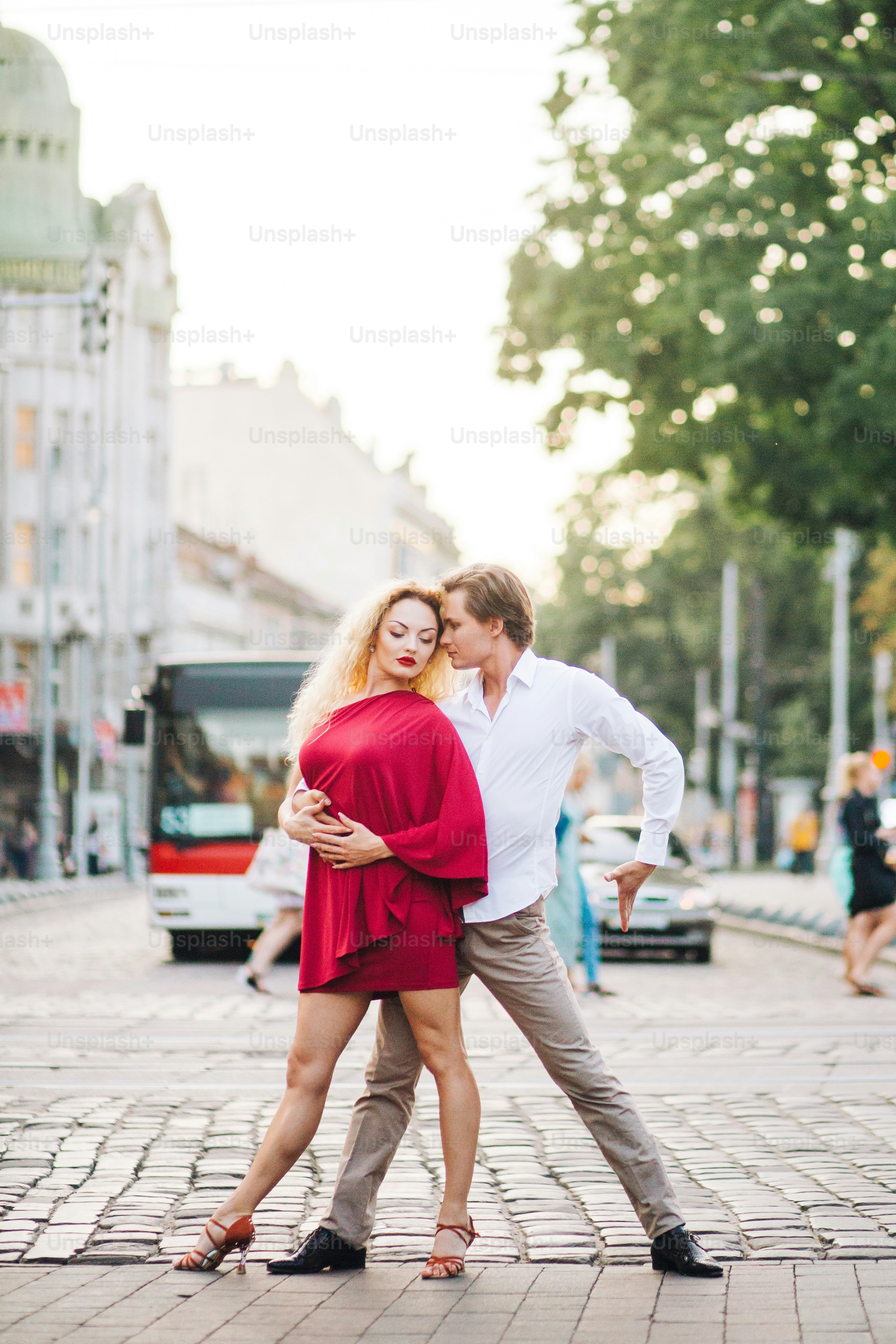 Foto Casal hipster apaixonado dançando nas ruas, lua de mel de verão do casal de dançarinos em elegante vestido vermelho e camisa branca, homem e mulher dançando tango ao ar livre – foto