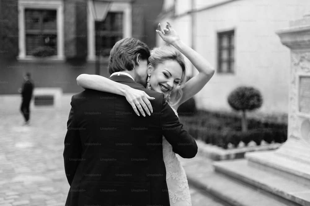 Retrato de pareja emocional, novia y novio felices y sonrientes abrazándose y riendo al aire libre, momento único de la boda
