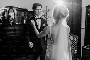 Happy newlywed couple, romantic smiling groom looking at gorgeous bride in elegant white wedding dress indoors in hotel