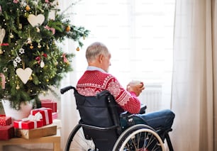 A senior man in wheelchair holding a cup of tea or coffee at home at Christmas time.