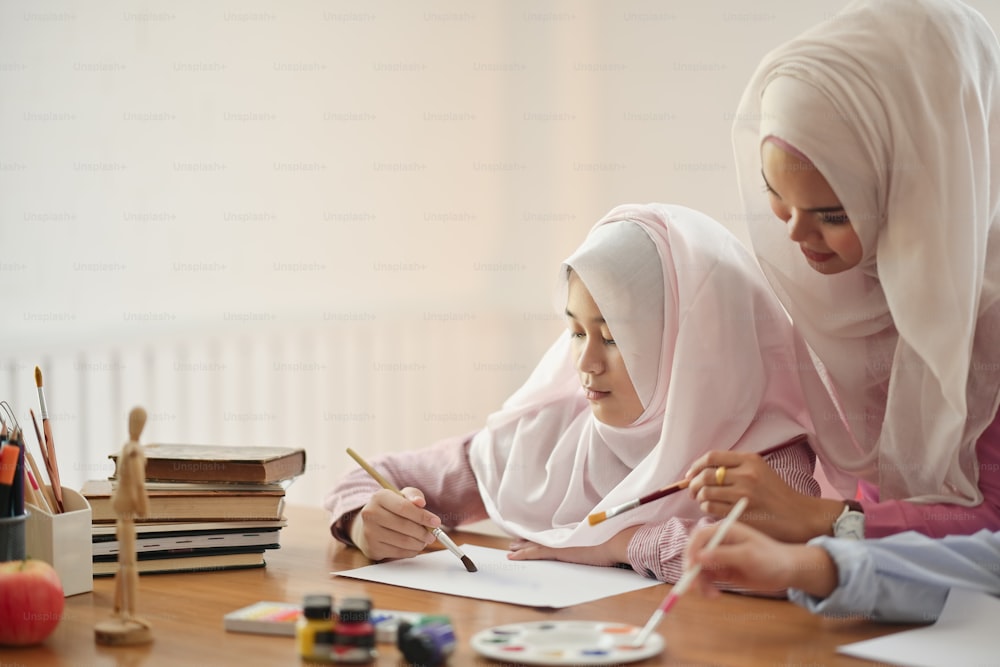 美術の授業で生徒に絵を教える若いアジアのイスラム教徒のヒジャーブ