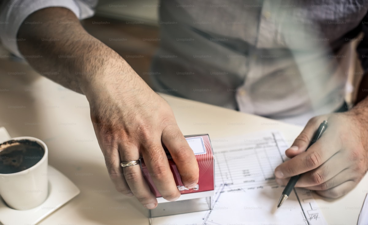 Hand stamping a permit document at a desk with a building plan, representing the building department approval step in the commercial permit process