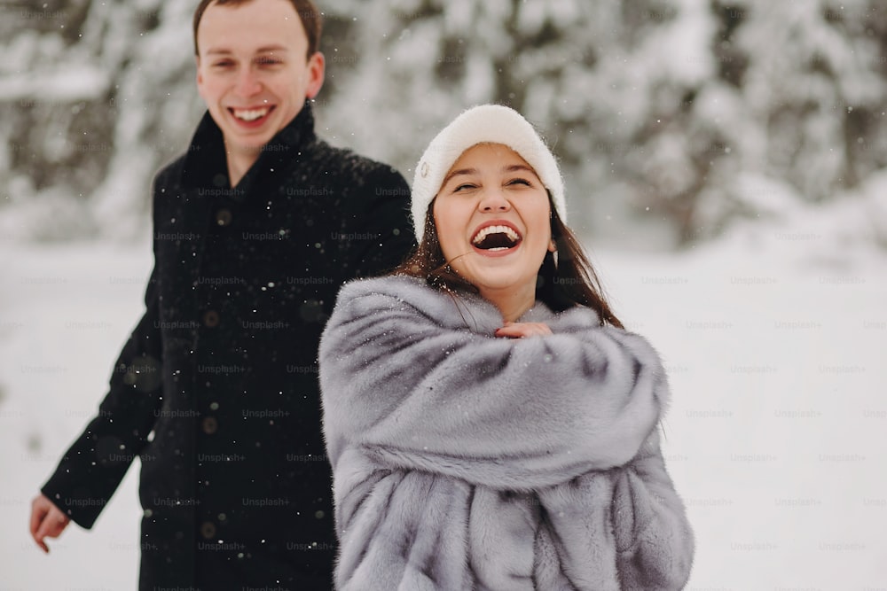 Stylish couple in love having fun in snowy mountains. Happy family playing in snow and smiling in winter mountains and forest. Holiday getaway together. Romantic moments