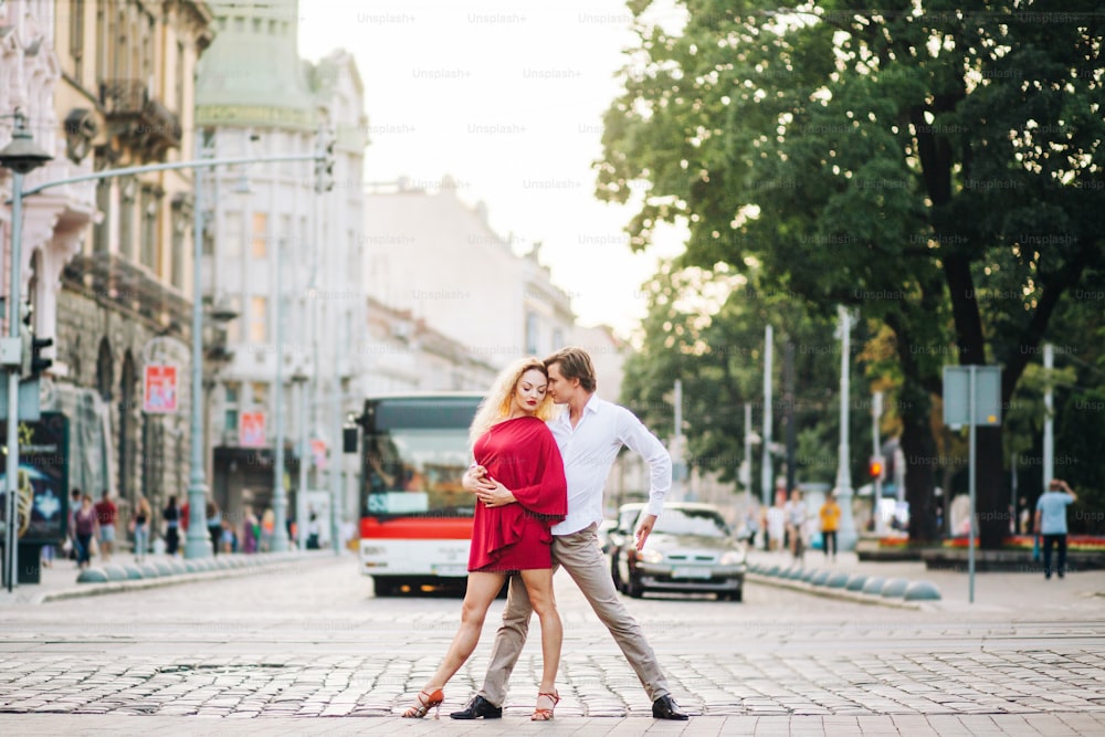 beautiful happy couple in love embracing and dancing in evening sunlight in sunny street. stylish hipster groom and blonde bride performing dance, professional dancers. romantic moments in summer