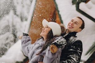 Stylish couple playing with snow in wooden cabin on background of winter snowy mountains. Happy joyful family having fun and smiling in snow. Emotional funny moments together