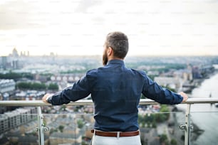 Eine Rückansicht des Hipster-Geschäftsmannes, der vor London steht, sieht das Panorama bei Sonnenuntergang.