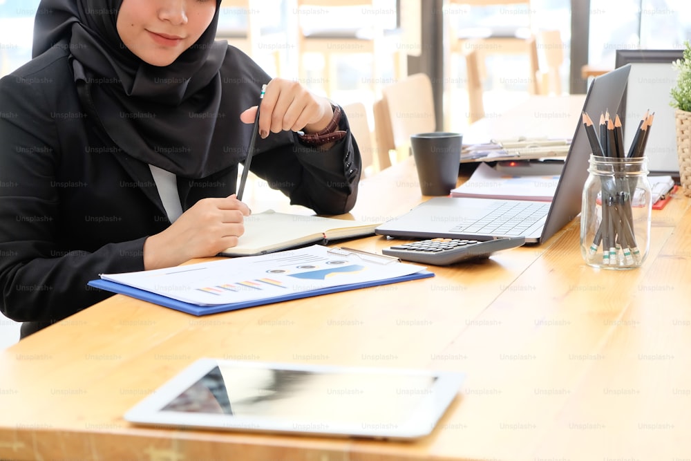 Mulher islâmica que trabalha com papel de relatório de dados financeiros de finanças.