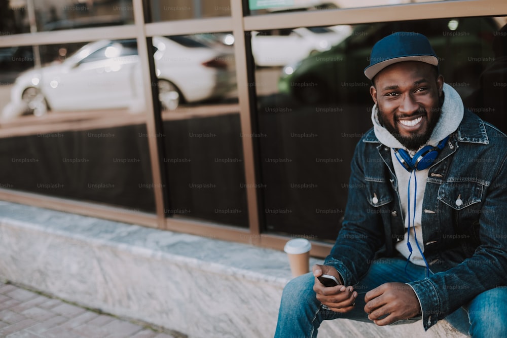 Cheerful handsome afro american man using his phone while sitting in the city