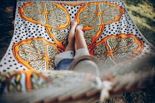 화창한 여름 공원에서 해먹에 있는 세련된 힙스터 여자 다리. 숲에서 쉬고 있는 금발 소녀, 웃으며 하루를 즐기고 있다. 여름 방학, 텍스트를위한 공간. 캠핑