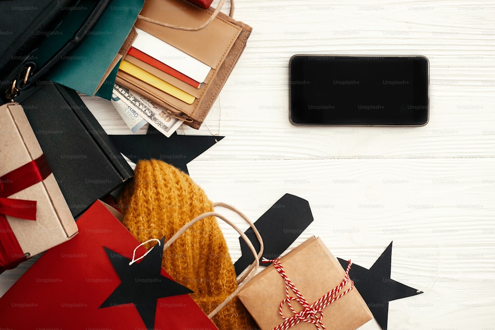 Christmas shopping and seasonal sale. Phone with empty screen, credit cards, money, wallet,  bags, clothes, gift boxes, tags on rustic wood. Space for text. Advertising app