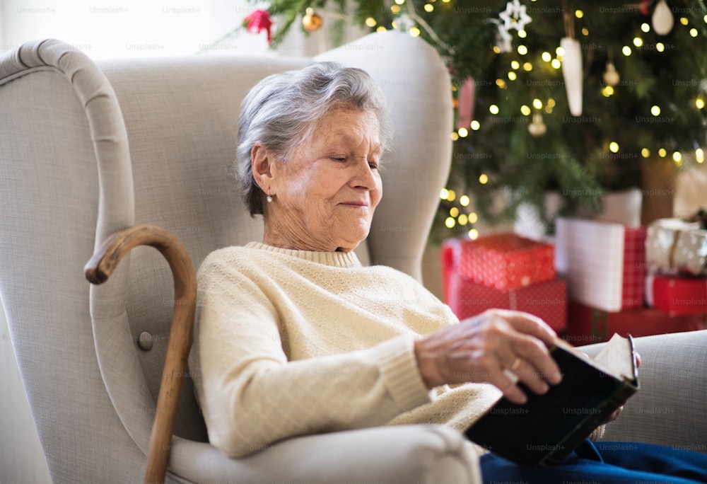 Uma mulher idosa solitária sentada em uma poltrona em casa na época do Natal, lendo a Bíblia.