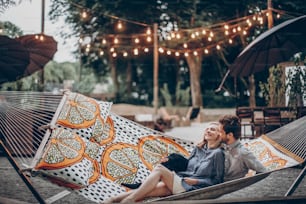 Romantisches Hipster-Paar genießt Ruhe in einer Hängematte im Park Resort, süße Frau liegt mit gutaussehendem Mann, Lichter im Hintergrund