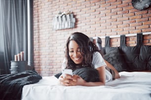 Portrait of beautiful woman waking up in her bed and looks into the phone. Check social networks, send sms. The girl is wearing a T-shirt.