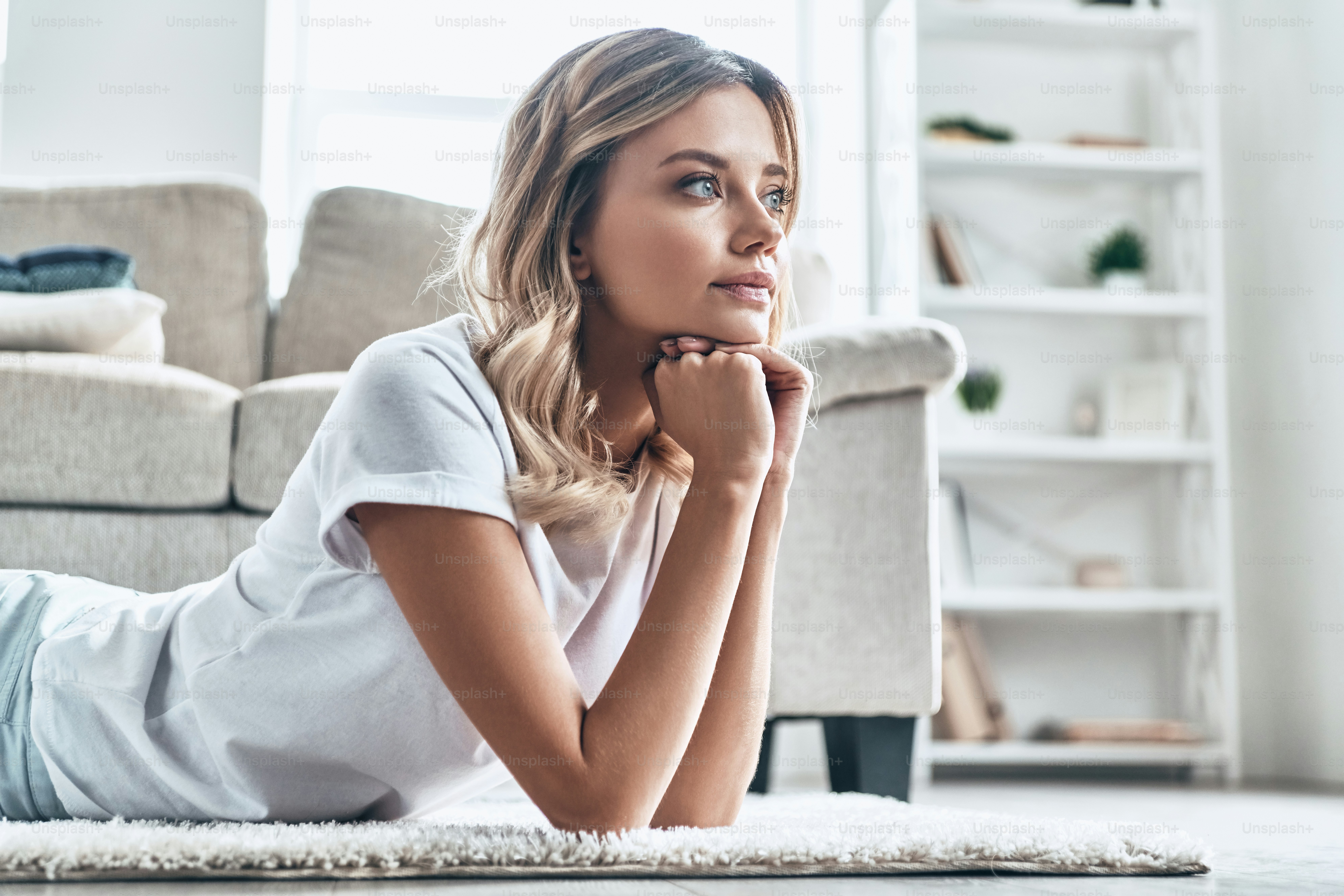 Bella giovane donna che distoglie lo sguardo e sorride mentre si trova sul pavimento di casa
