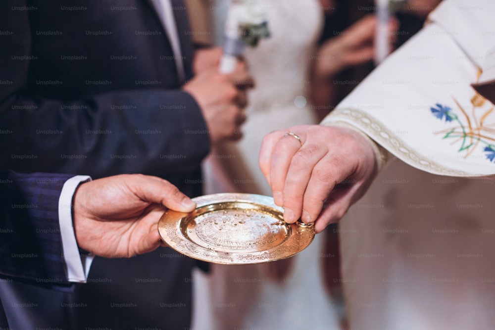 Priester vergoldet goldene Eheringe auf dem Teller in der Kirche bei der Hochzeit Ehe. Traditionelle religiöse Hochzeitszeremonie