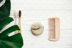 Zero waste concept. Natural eco friendly bamboo toothbrushes, solid shampoo bar, brush,  soap on white wood with green monstera leaves. Eco products plastic free. Hygiene care and treatment