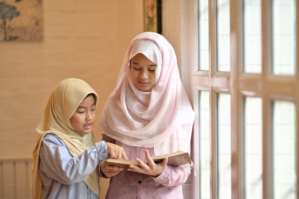 Two young Asian Muslim girls reading a book together.