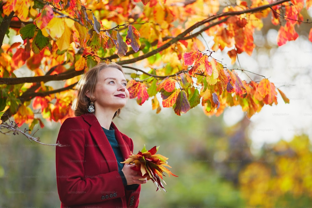Beautiful young woman with bunch of colorful autumn leaves walking in park on a fall day