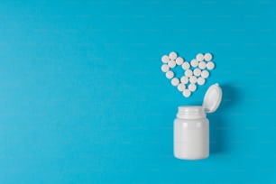 青い背景にハート型の薬の丸薬。心臓の保護。治療薬の処方箋。薬剤の薬物、健康のための容器の治療。上面図。フラットレイ。