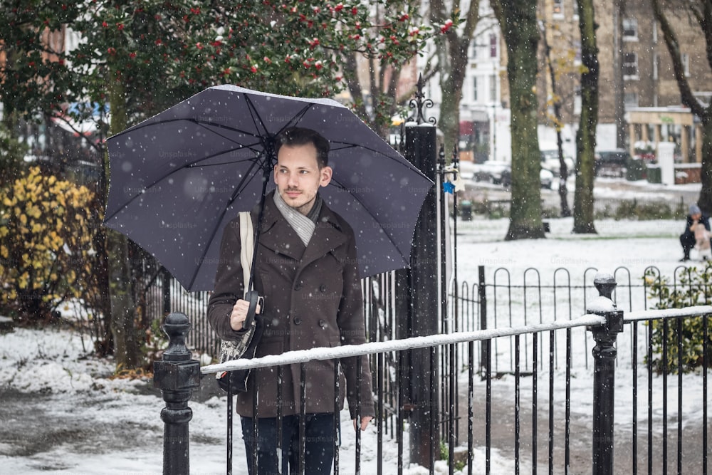 Porträt eines gutaussehenden jungen Mannes mit Regenschirm auf der Londoner Straße im Winterschnee