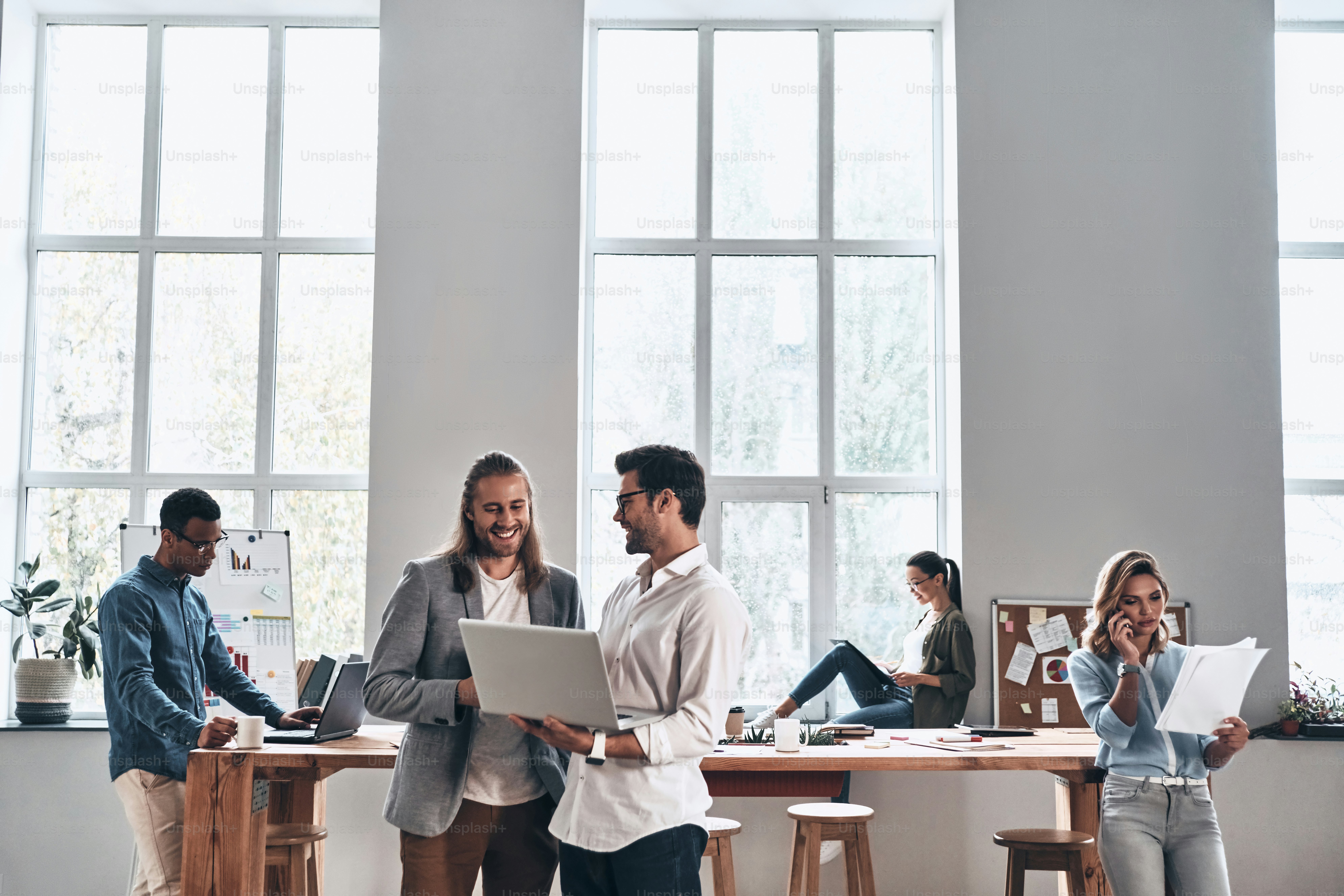 Group of young modern people in smart casual wear smiling and discussing something while working in the creative office