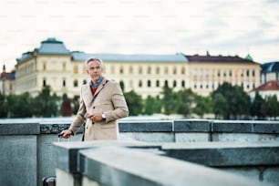 Hombre de negocios guapo maduro con maleta y teléfono inteligente parado en un puente en la ciudad de Praga. Espacio de copia.