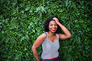 A portrait of a black laughing woman standing against green background of bush leaves.