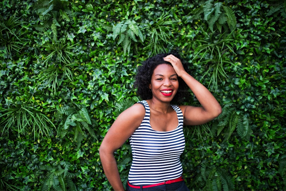 A portrait of a black laughing woman standing against green background of bush leaves.