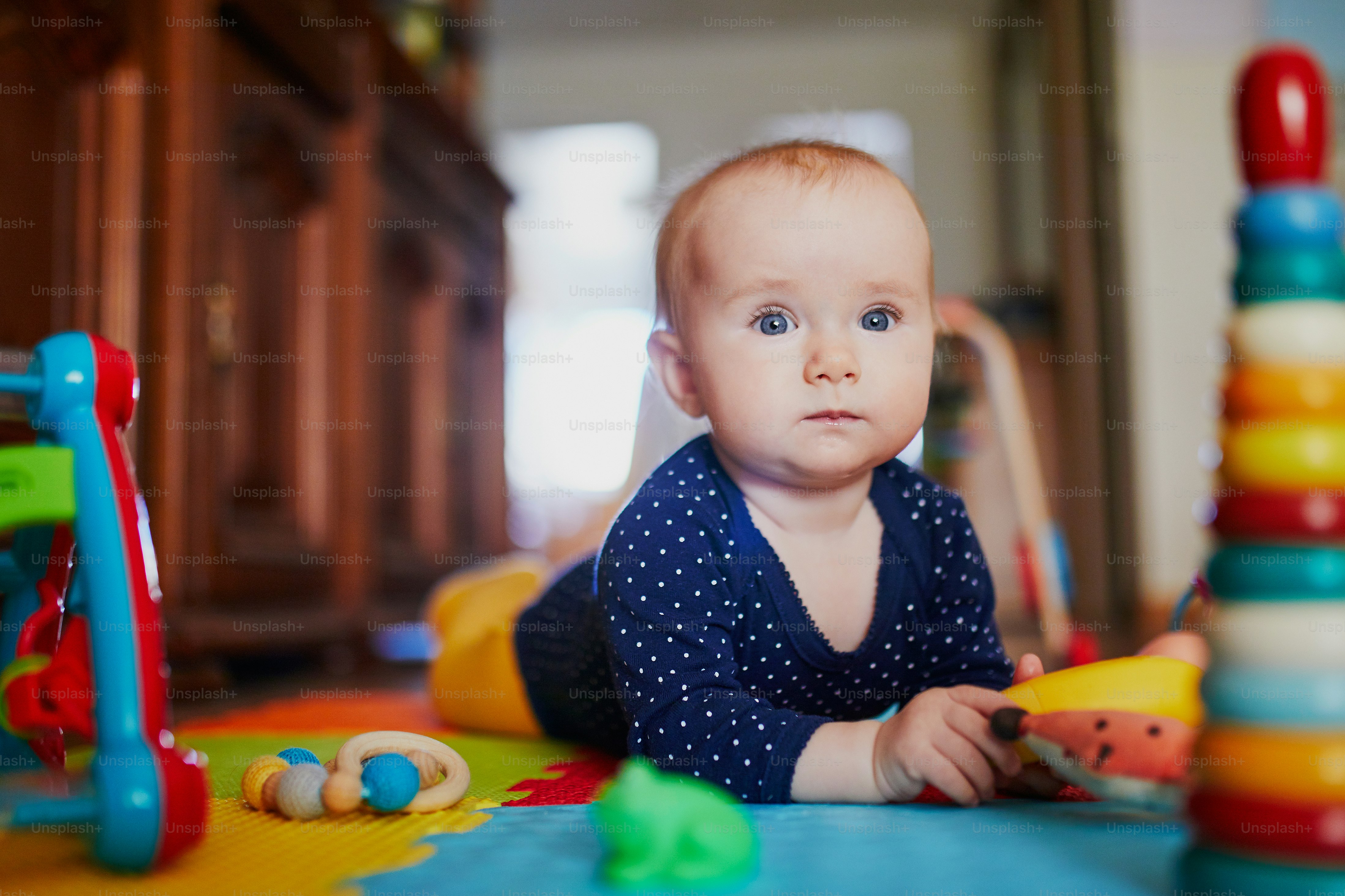 Baby Mädchen spielt mit Spielzeug auf dem Boden. Glückliches, gesundes kleines Kind zu Hause