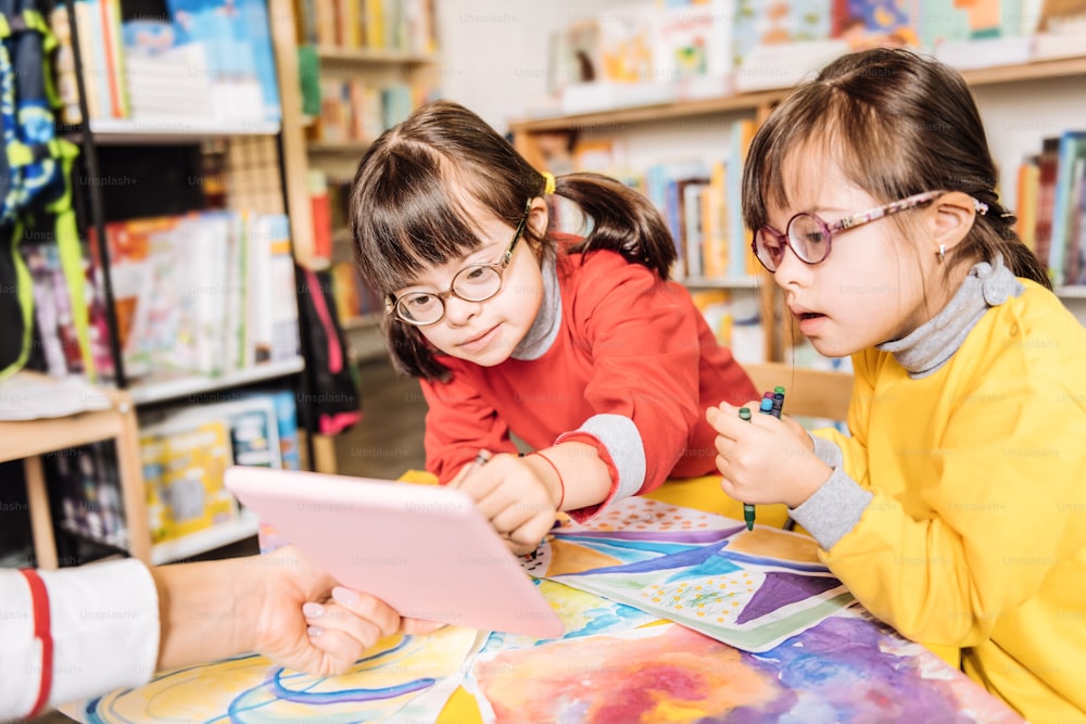 Drawing class. Dark-haired appealing preschool girls with Down syndrome having drawing class