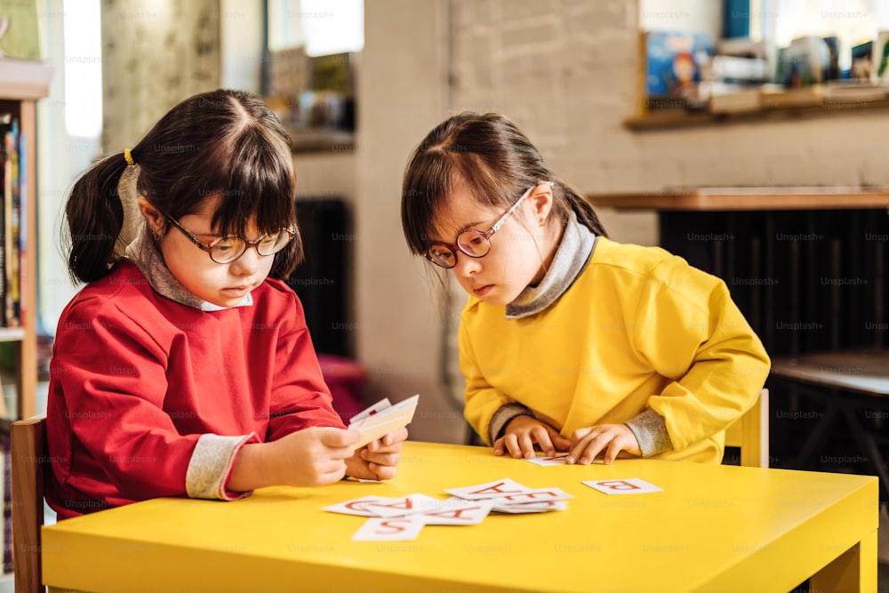 Tarjetas de aprendizaje. Dos niños agradables, encantadores y soleados que se sienten involucrados en mirar tarjetas de aprendizaje