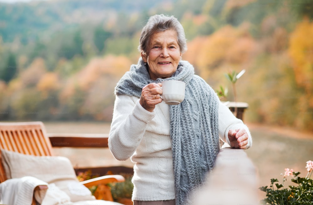 Eine ältere Seniorin sitzt an einem sonnigen Herbsttag draußen auf einer Terrasse.