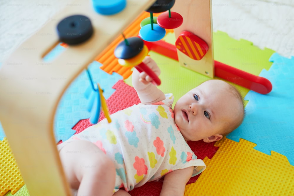 カラフルなプレイマットの上でおもちゃを楽しんでいます愛らしい女の子の赤ちゃん。床で遊んで幸せな健康な子供