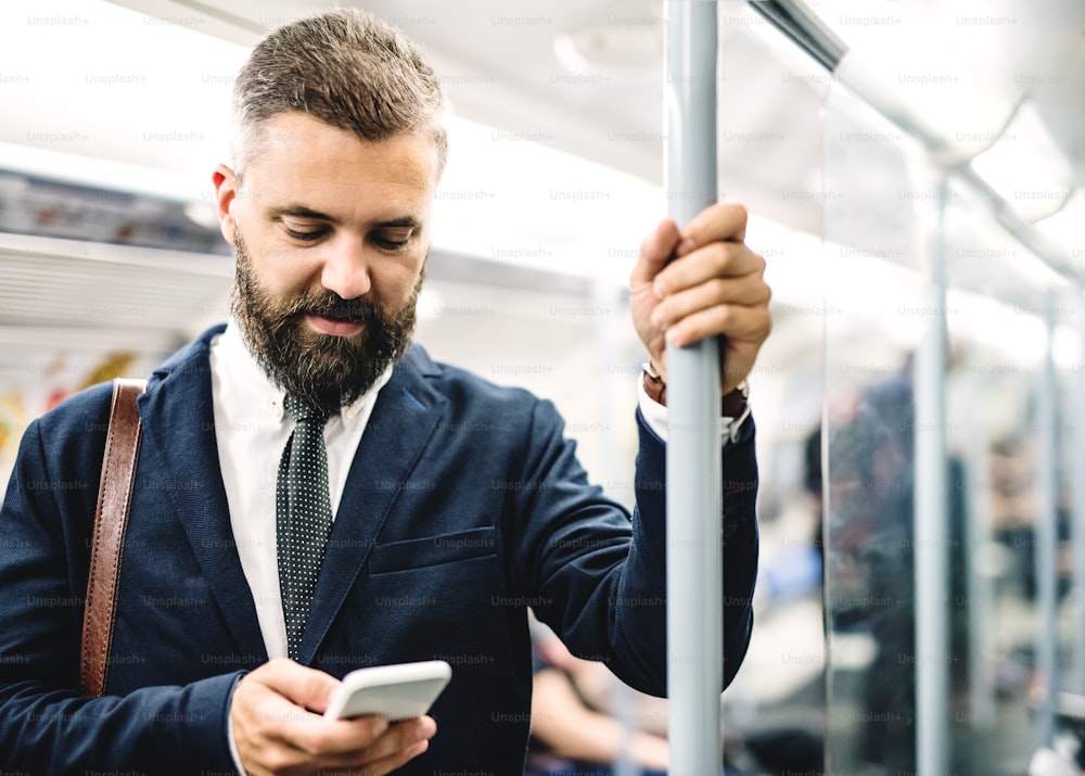 Hipster businessman with smartphone sitting inside the subway in the city, travelling to work.