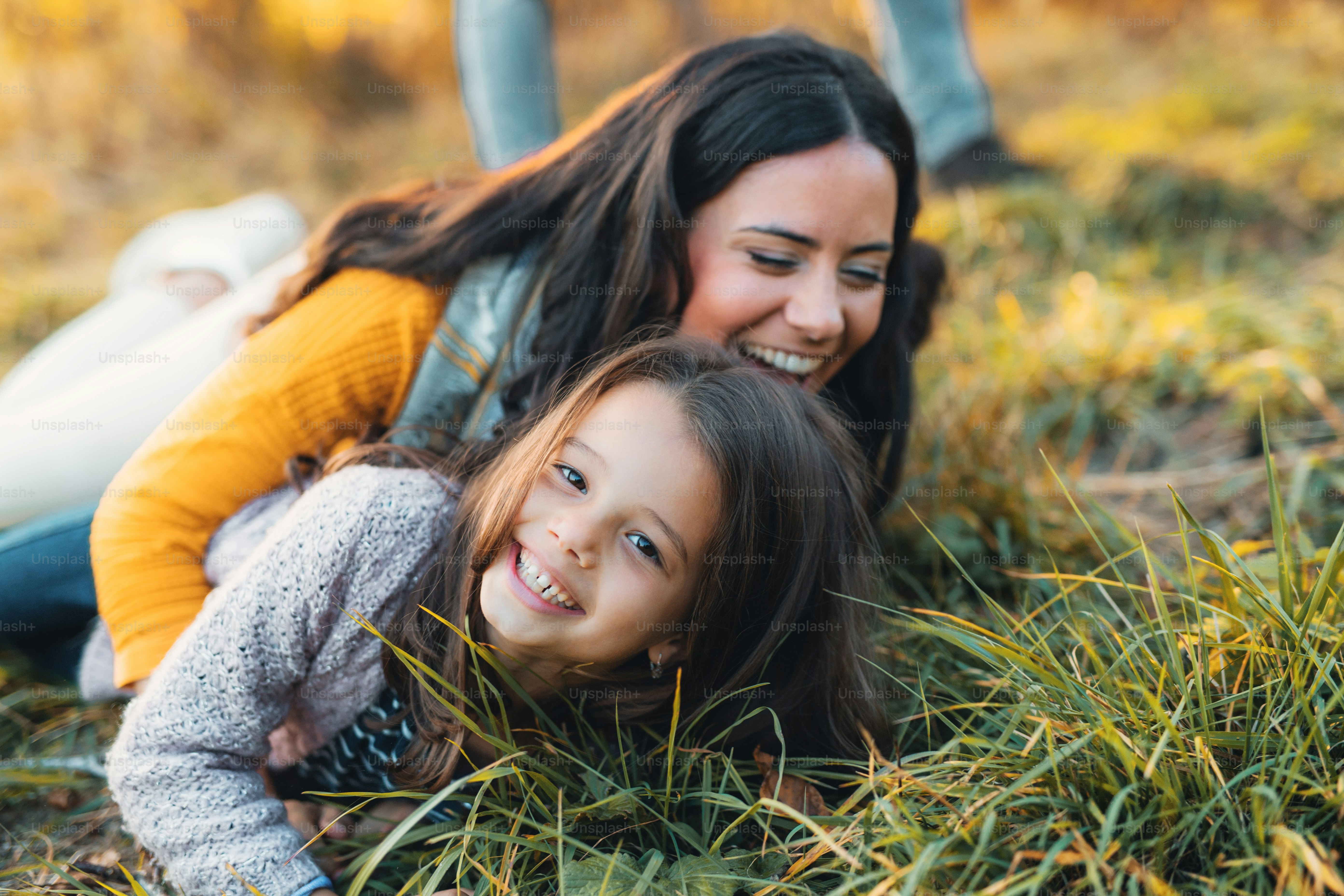 Um retrato de uma jovem mãe com uma filha pequena deitada em um chão na natureza do outono.