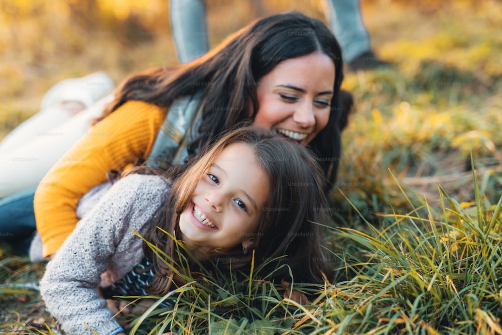 A portrait of young mother with a small daughter lying on a ground in autumn nature.