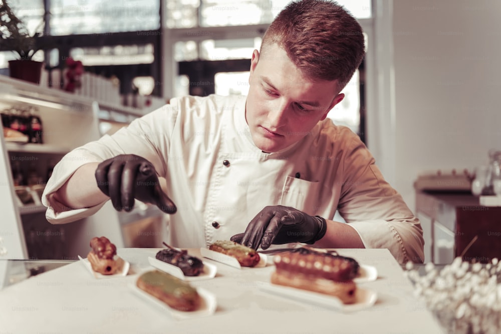 Real professional. Serious skilled pastry chef focusing on his work while preparing eclairs