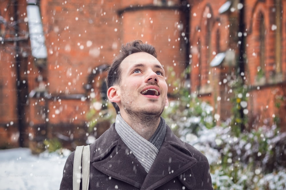 Porträt eines glücklich lächelnden Mannes, der im Winter über fallenden Schnee erstaunt ist
