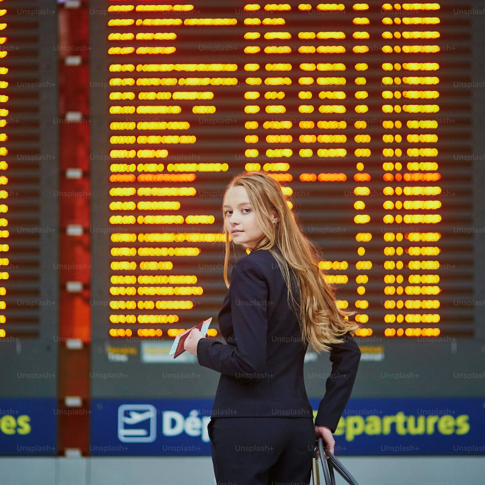 Junge Frau auf internationalem Flughafen in der Nähe eines großen Informationsdisplays