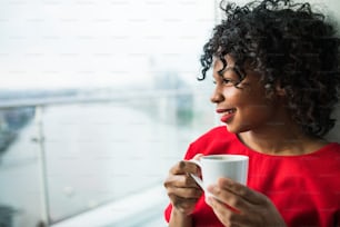 Gros plan d’une femme debout près de la fenêtre tenant une tasse de café. Espace de copie.