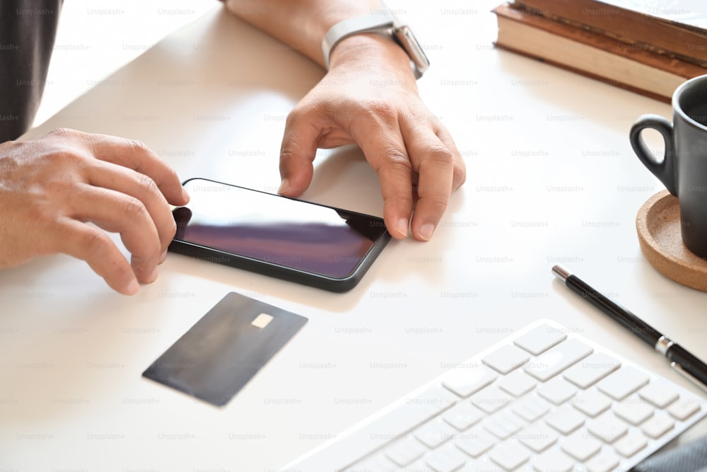 Hombre irreconocible usando el teléfono móvil y la tarjeta de crédito para el pago en línea