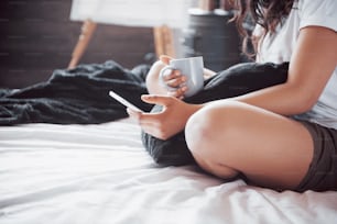 Portrait of beautiful woman waking up in her bed and looks into the phone. Check social networks, send sms. The girl is wearing a T-shirt.